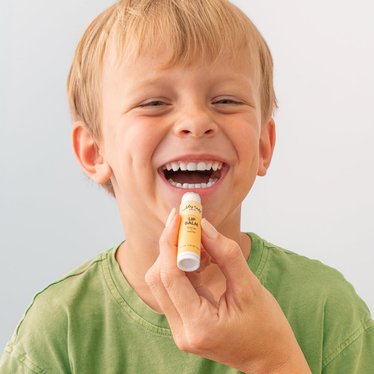 Mama holding a lip balm applying to her son's smiling lips